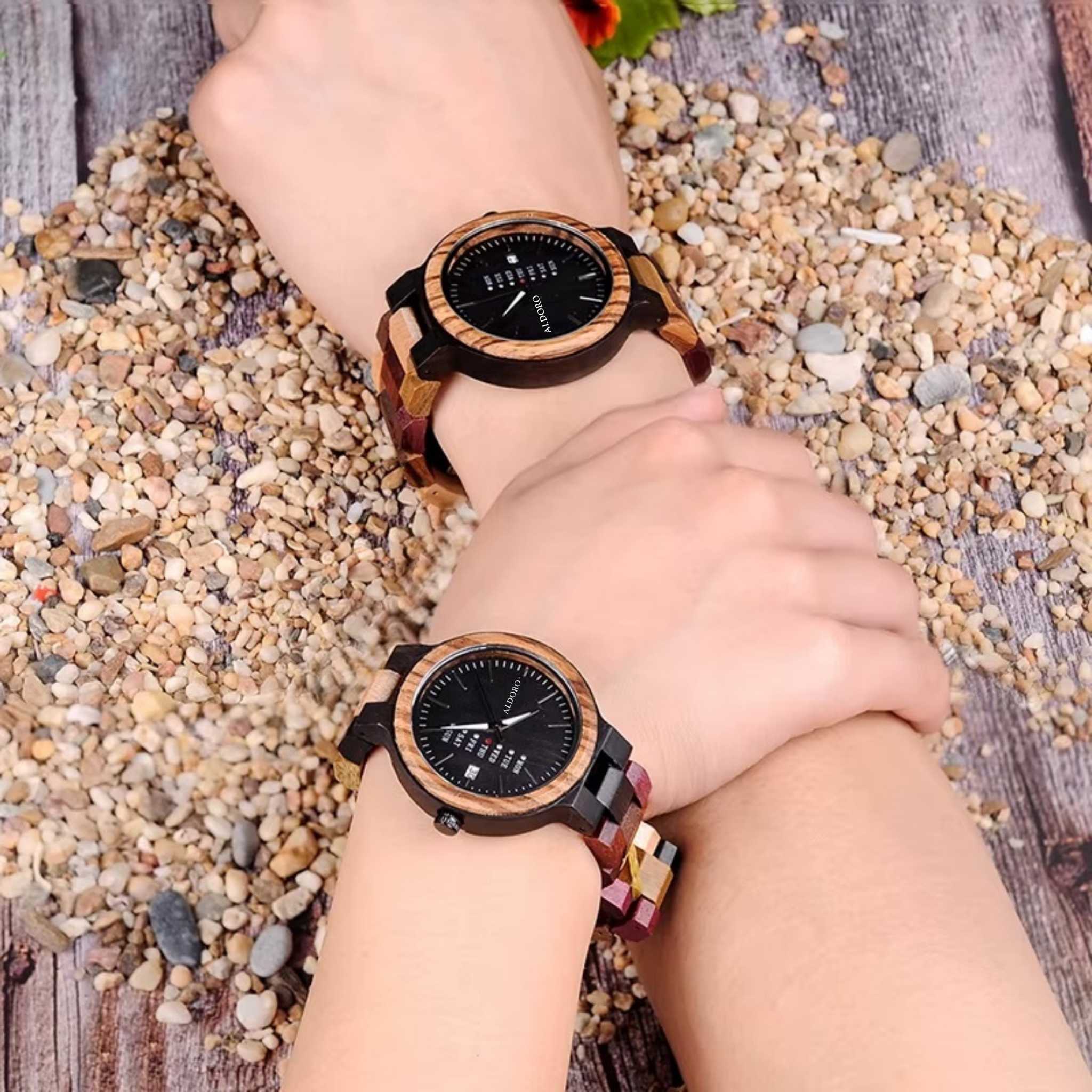 Two intertwined wrists wearing luxury wooden watches by Aldoro Watches, symbolizing connection, shared moments, and the essence of The Aldoro Story, set against a natural pebbles and wood background.